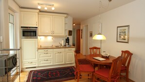 A kitchen with white cabinets, a microwave, and a dining area with wooden chairs and a table. - Ferienoase Usedom (Heringsdorf)