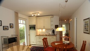 A compact kitchen with white cabinets, a microwave, and a dining area with a wooden table and chairs. - Ferienoase Usedom (Heringsdorf)