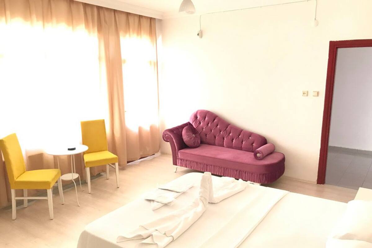 Una habitación de hotel con una cama, un sofá morado, dos sillones amarillos y una pequeña mesa.