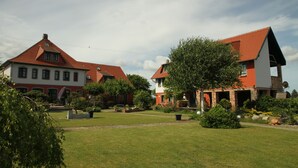 A residential area with two houses, one with a red roof and white walls, and another with a red roof and white walls. There is a well-maintained lawn and a variety of trees and shrubs.