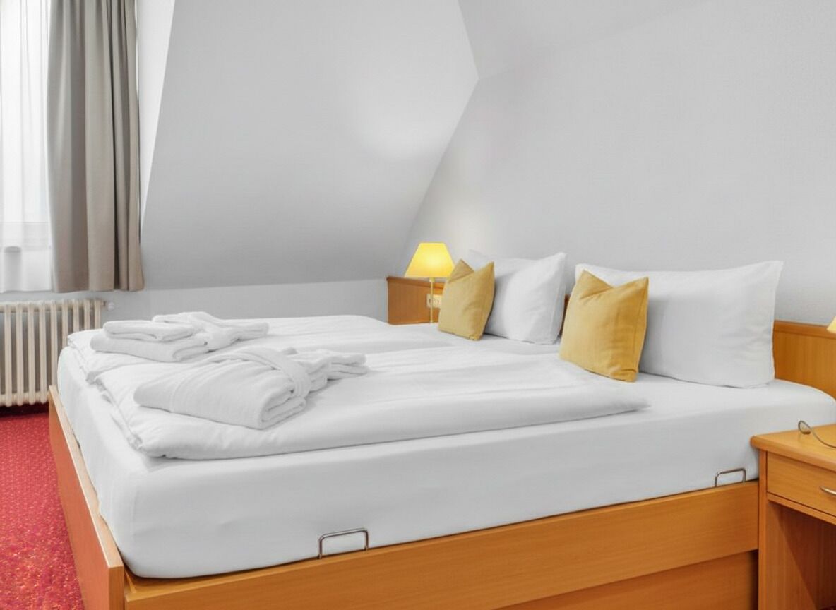 A neatly made bed with white linens and a lamp on the bedside table.