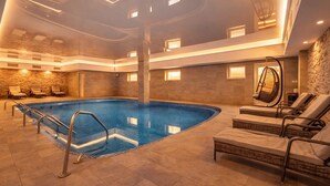 A large indoor swimming pool with a modern design, surrounded by lounge chairs and a stone wall. - Lázeňský Hotel Pyramida I (Frantiskovy Lazne)