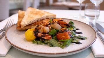 A plate of food with grilled shrimp, lemon, and greens, accompanied by a slice of bread on a table.