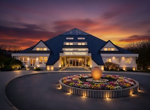A modern hotel with a prominent entrance, a well-lit facade, and a circular flower bed in the foreground. - Lázeňský Hotel Pyramida I (Frantiskovy Lazne)