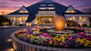 A hotel with a modern design, a large vase in the center of a flower bed, and a sign that reads 'HOTEL PYRAMIDA.'