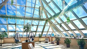 A spacious atrium with a high glass ceiling, multiple seating areas, and potted plants. - Lázeňský Hotel Pyramida I (Frantiskovy Lazne)