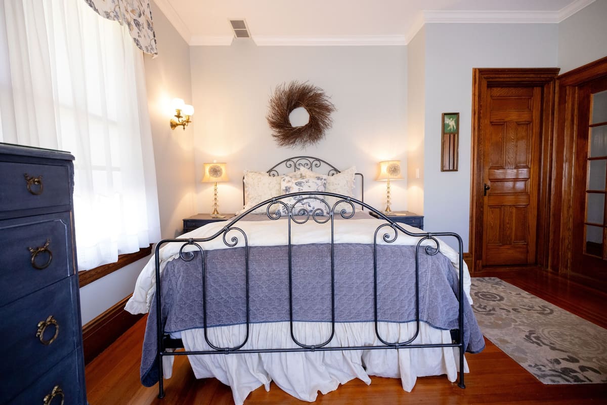 A bedroom with a metal bed frame, a dresser with drawers, a wall-mounted light fixture, and a wooden door.