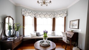 A room with a bay window, a round table, a dresser, a chair, and a mirror. - Circular Manor Bed and Breakfast (Saratoga Springs)