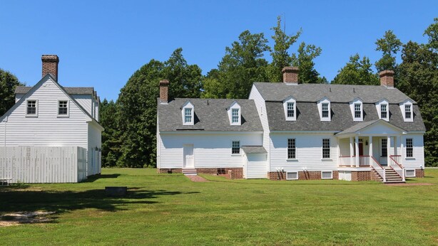 A large white house with a front porch and multiple chimneys, surrounded by a grassy field and trees.