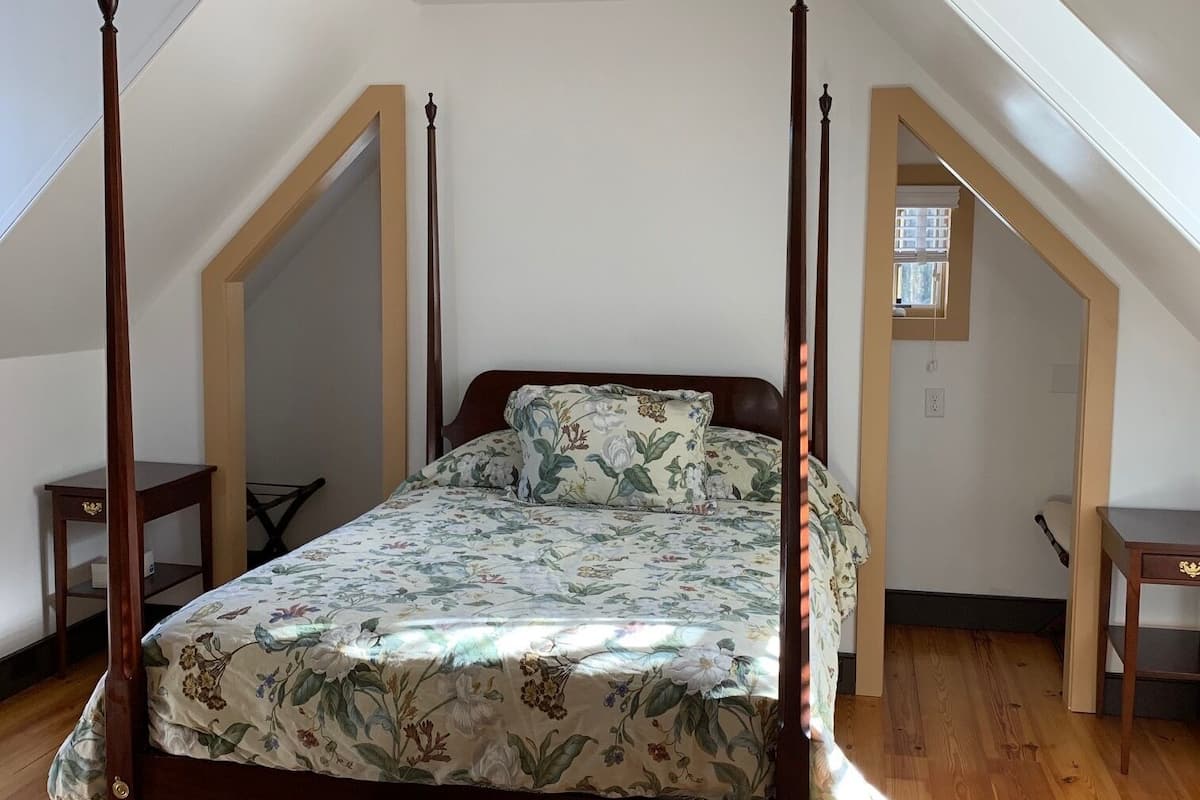 A bedroom with a four-poster bed, wooden flooring, and a sloped ceiling.