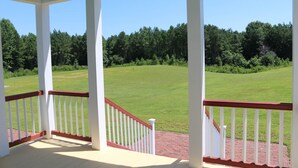 A covered porch with white railings and a brick pathway leading to a grassy field.