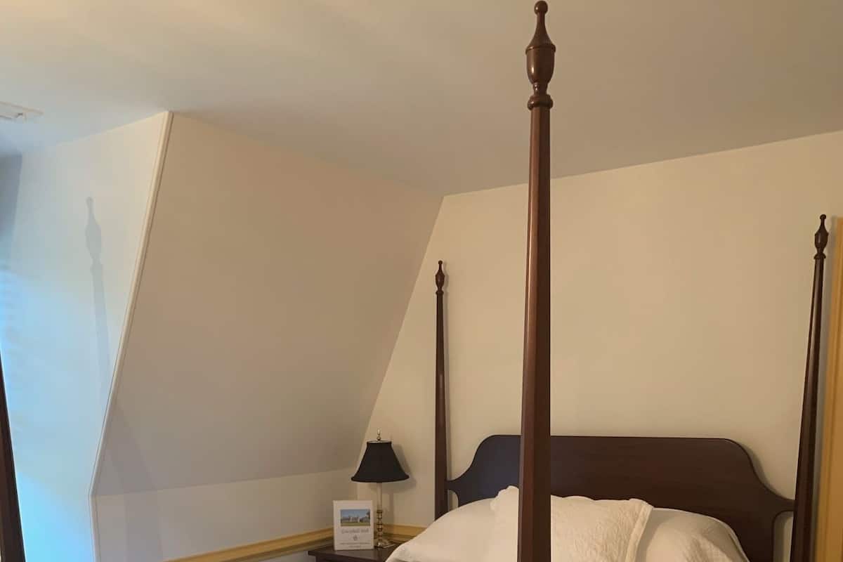 A four-poster bed with a white quilt, a nightstand with a lamp, and a framed picture on the wall.