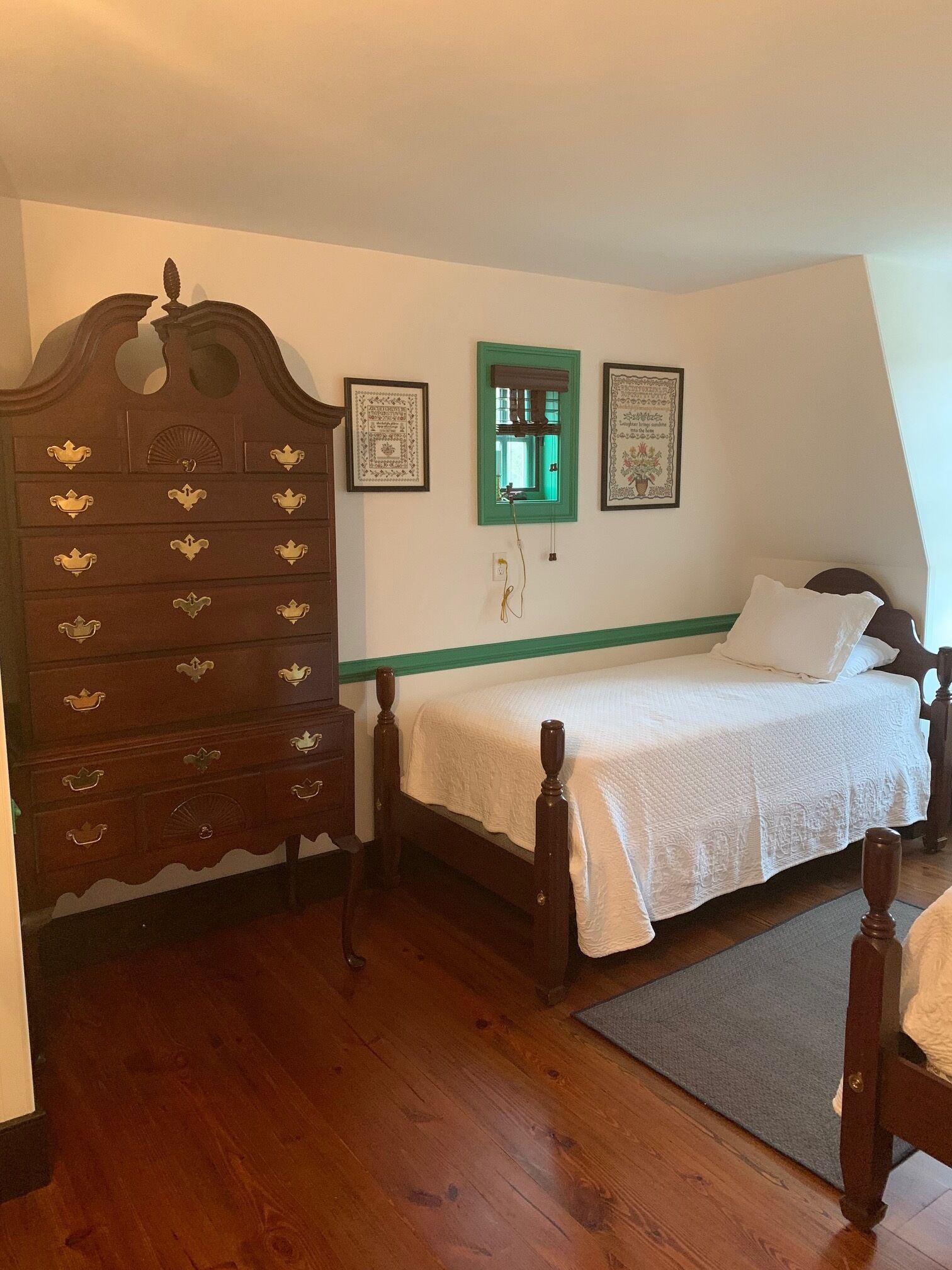 Un dormitorio con un aparador de madera, una cama con cabecera verde y dos cuadros en la pared.