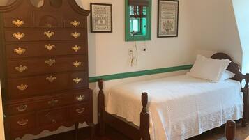 Un dormitorio con un aparador de madera, una cama con cabecera verde y dos cuadros en la pared.