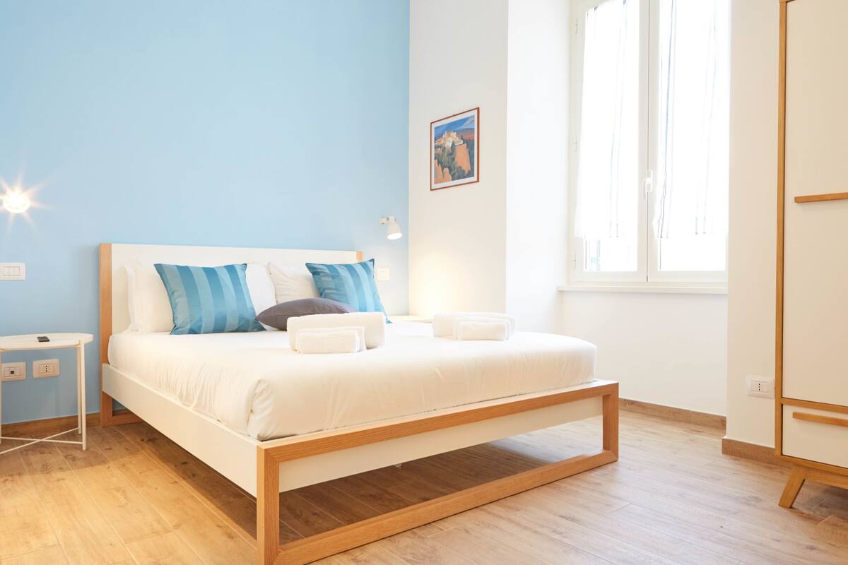 A modern bedroom with a wooden bed frame, white bedding, and a blue accent wall.