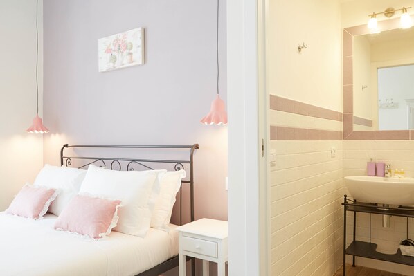 Une chambre à coucher avec un lit, une table de chevet et une salle de bain équipée d’un lavabo et d’un miroir.