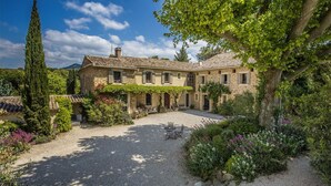 A stone house with a courtyard, surrounded by lush greenery and flowering plants.