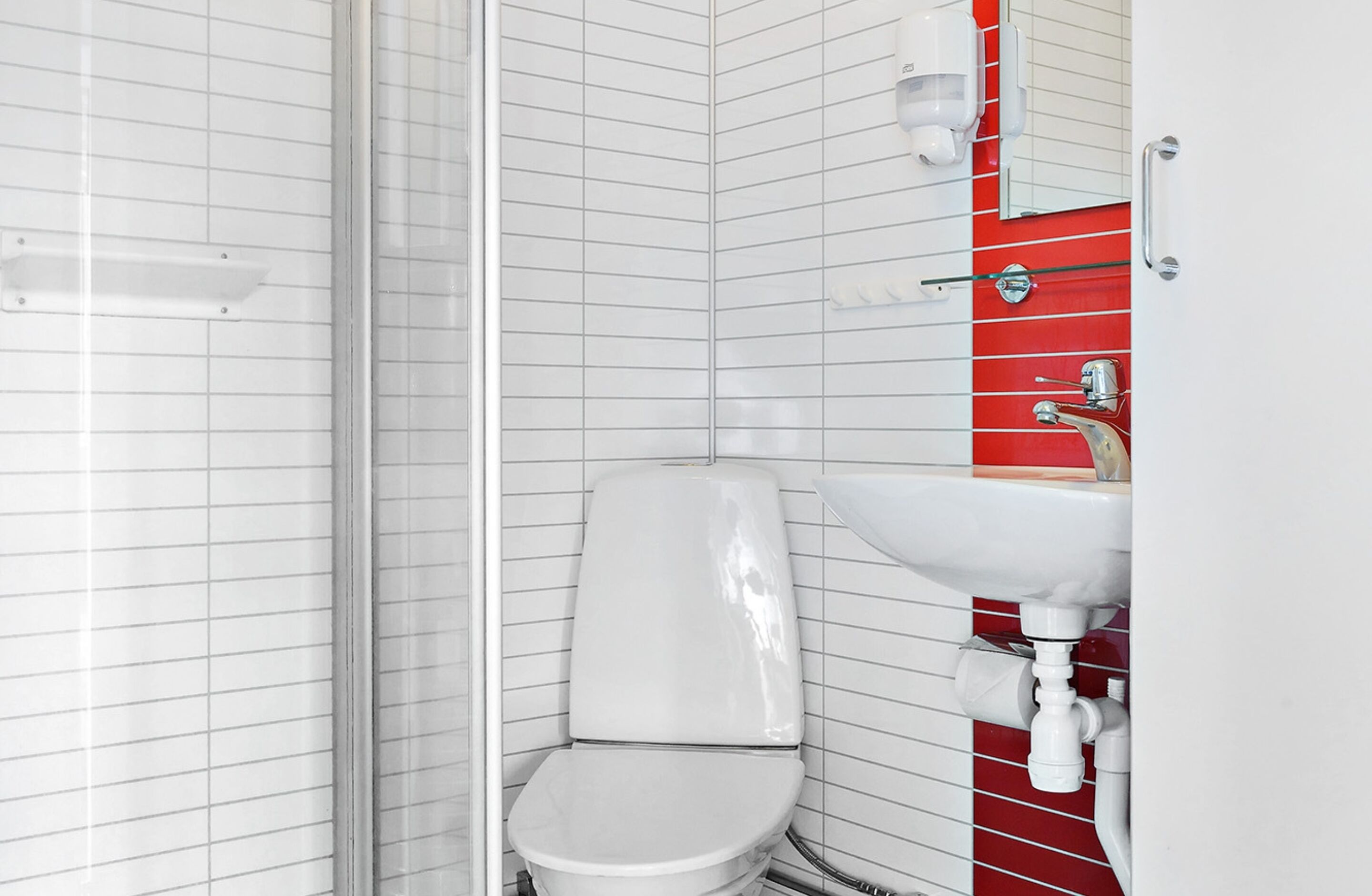 A bathroom with a white toilet, a red tiled wall, and a white sink with chrome fixtures.