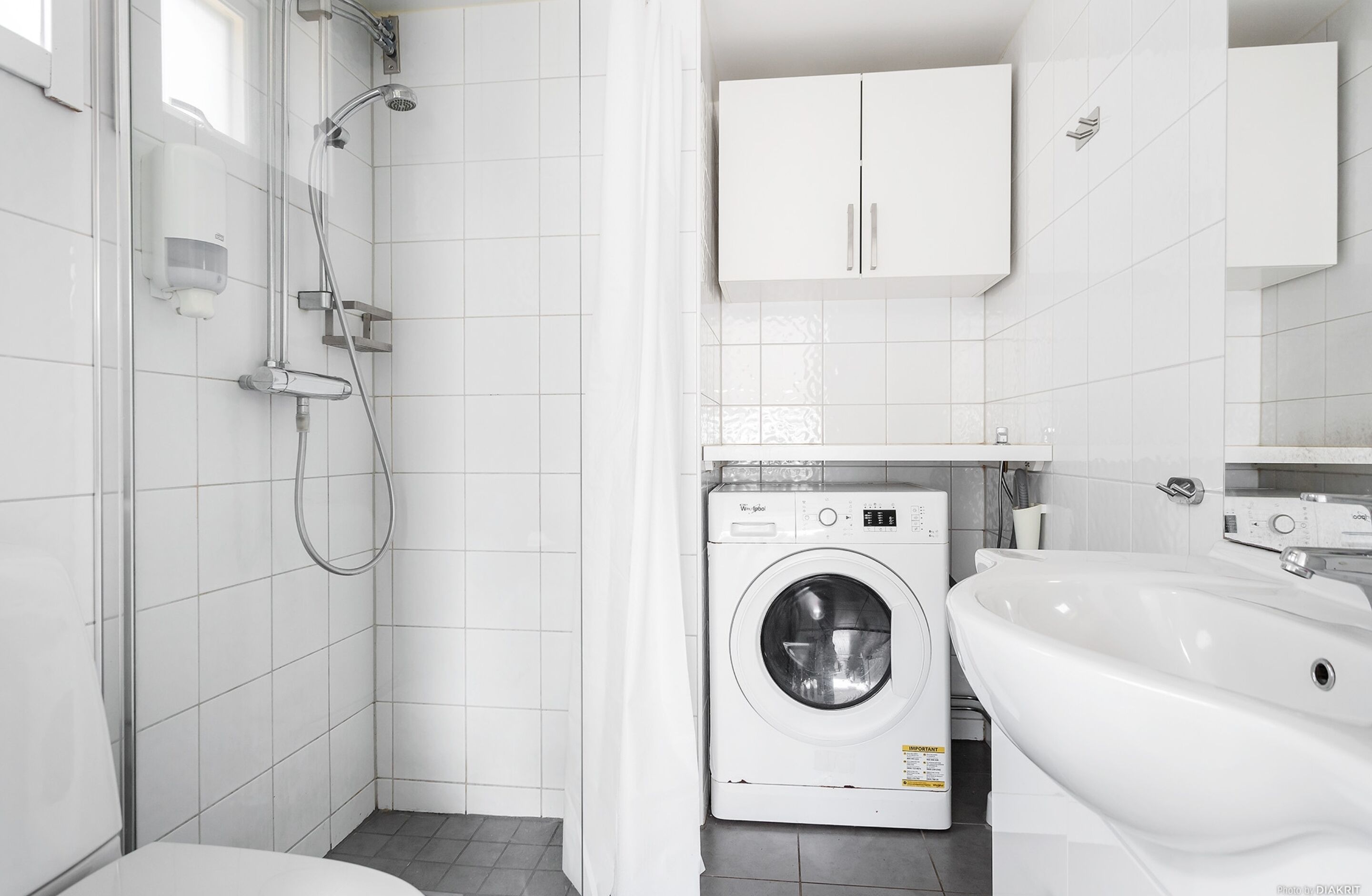Een moderne badkamer met douche, toilet, wasmachine en wastafel.