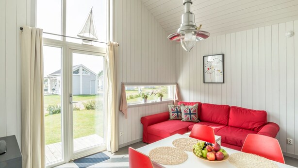 A bright room with a red sofa, a dining table with fruit, and a view of a garden through large windows. - First Camp Råå Vallar Helsingborg (Råå)
