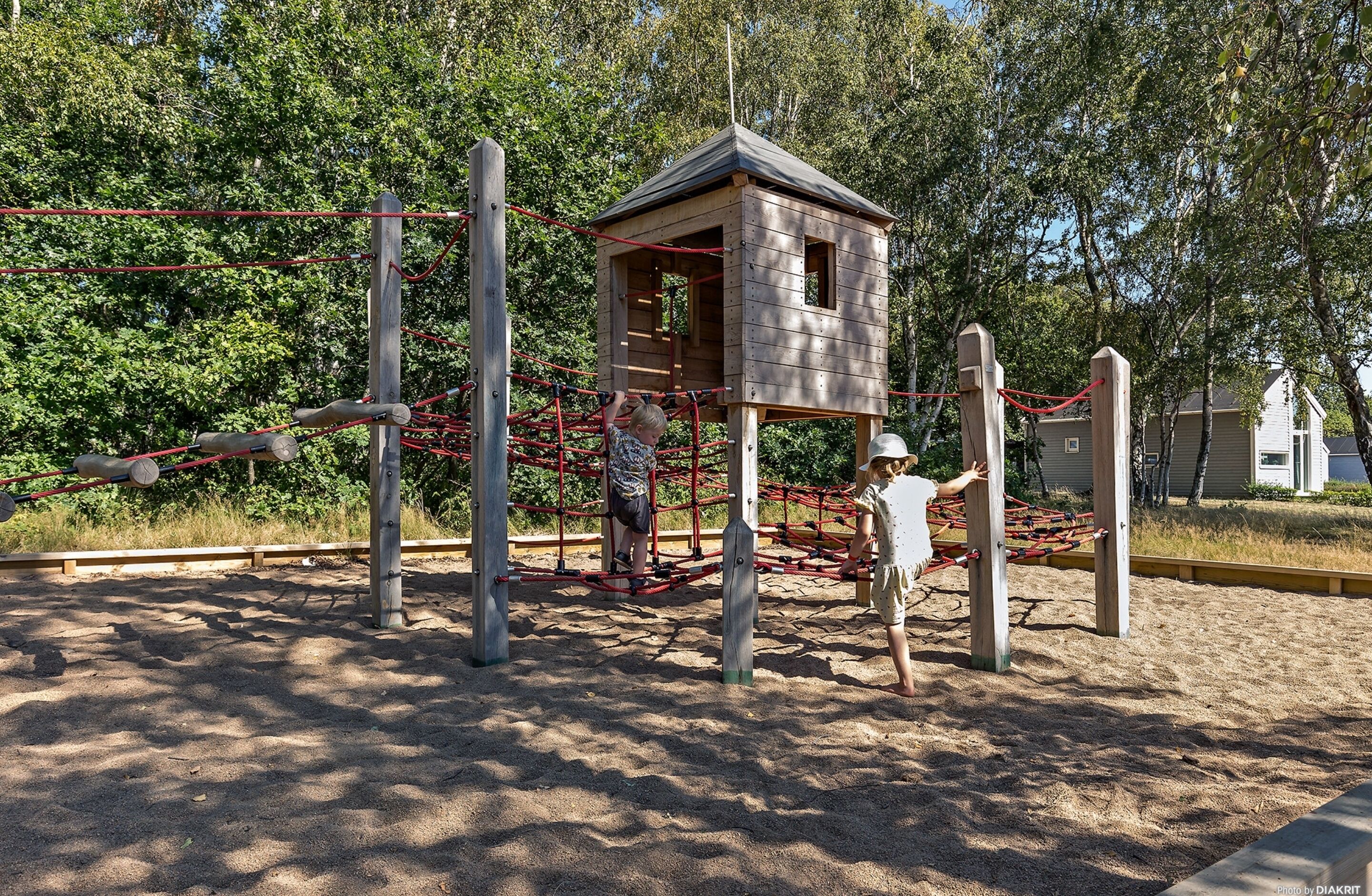 Un patio de juegos con una estructura de madera para escalar y una casita.