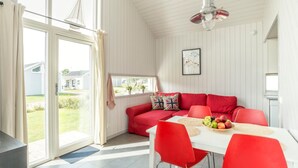 A bright room with a red sofa, a dining table with red chairs, and a view of a house through a glass door. - First Camp Råå Vallar Helsingborg (Råå)