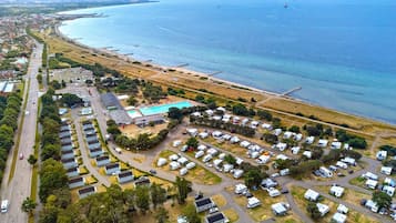 Vista aérea de un parque para vehículos recreativos en la costa, con varias autocaravanas, una piscina y una playa.