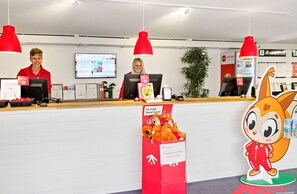 A reception desk with two staff members, a computer, and a large plush toy.