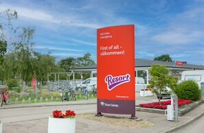 A red and white sign for First Camp Resort in Helsinki, with a clear view of bicycles and a parking area in the background.