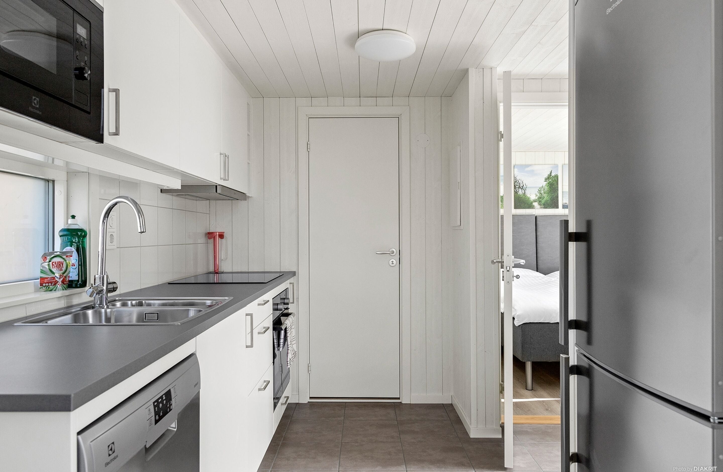 A compact kitchen with a dishwasher, a double sink, and a stainless steel refrigerator.