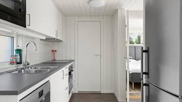 A compact kitchen with a dishwasher, a double sink, and a stainless steel refrigerator.
