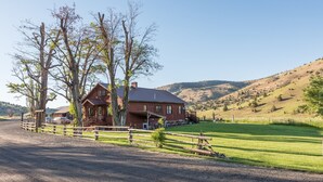 A rustic wooden house with a porch, surrounded by a fenced yard and a gravel driveway. - Wilson Ranches Retreat (Fossil)