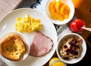 A breakfast plate with scrambled eggs, ham, toast, fruit, and oatmeal.