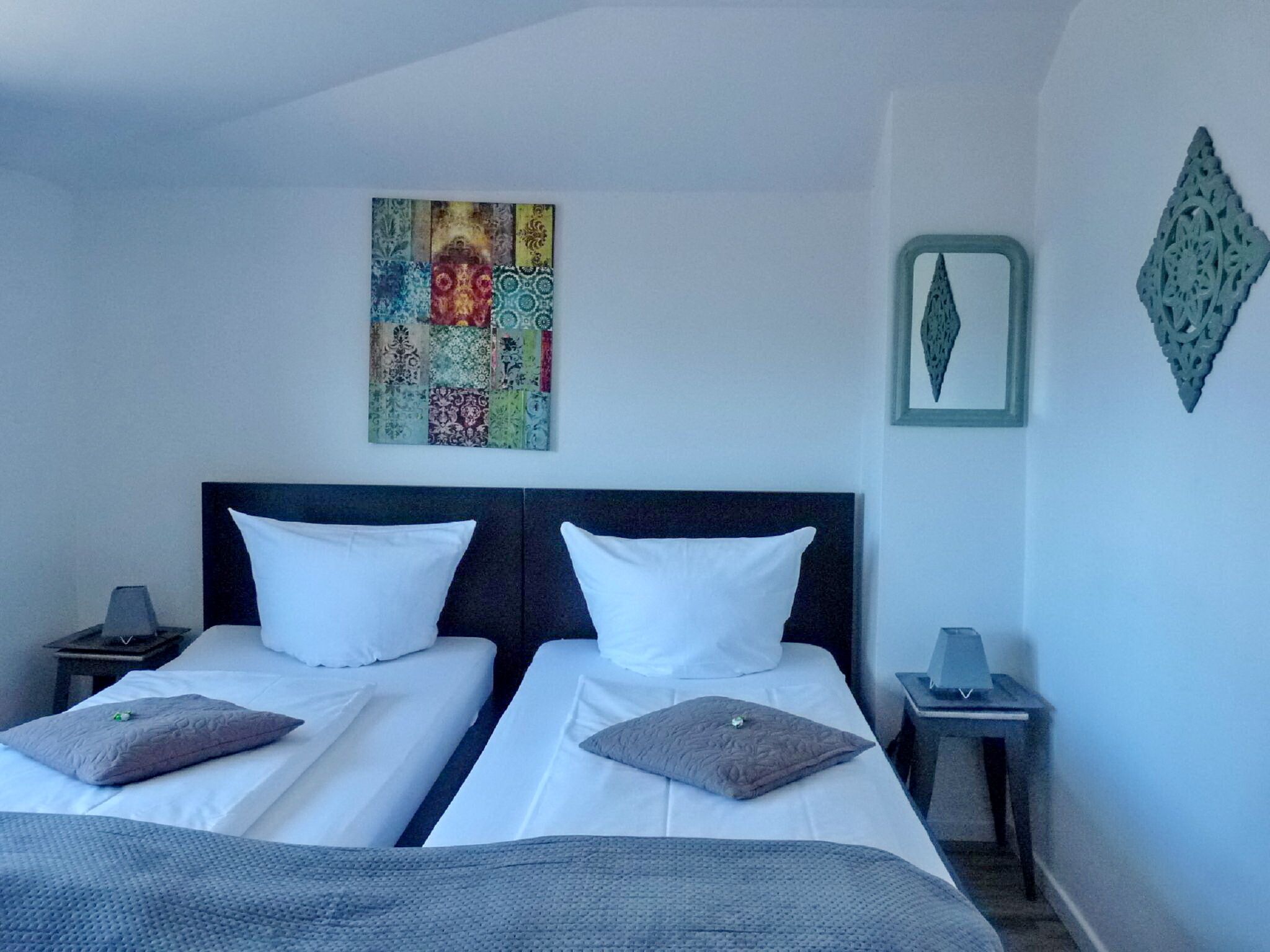 A hotel room with two single beds, a colorful artwork on the wall, and decorative wall pieces.