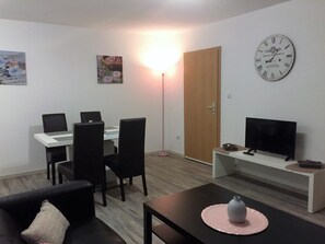 A modern living room with a dining area, a flat-screen TV, and a wall clock. - Haus am Burggraben (Hinte)