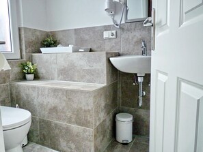A modern bathroom with a bathtub, sink, and toilet. - Haus am Burggraben (Hinte)