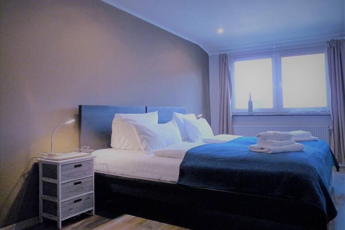 A hotel room with a bed, a nightstand, a lamp, a window with curtains, and a view of the city.