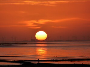 A sunset over a body of water with wind turbines in the background. - Haus am Burggraben (Hinte)