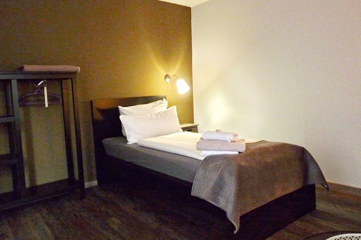 A hotel room with a bed, a nightstand, a lamp, and a wardrobe.
