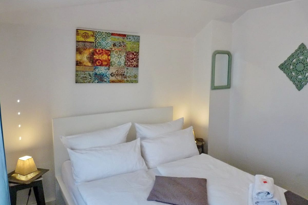 A hotel room with a bed, a nightstand, a lamp, a decorative wall piece, and a green wall ornament.