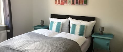 A neatly made bed with a grey and white duvet, two matching pillows, and a headboard. There are two bedside tables with lamps and a wall art piece above the bed.
