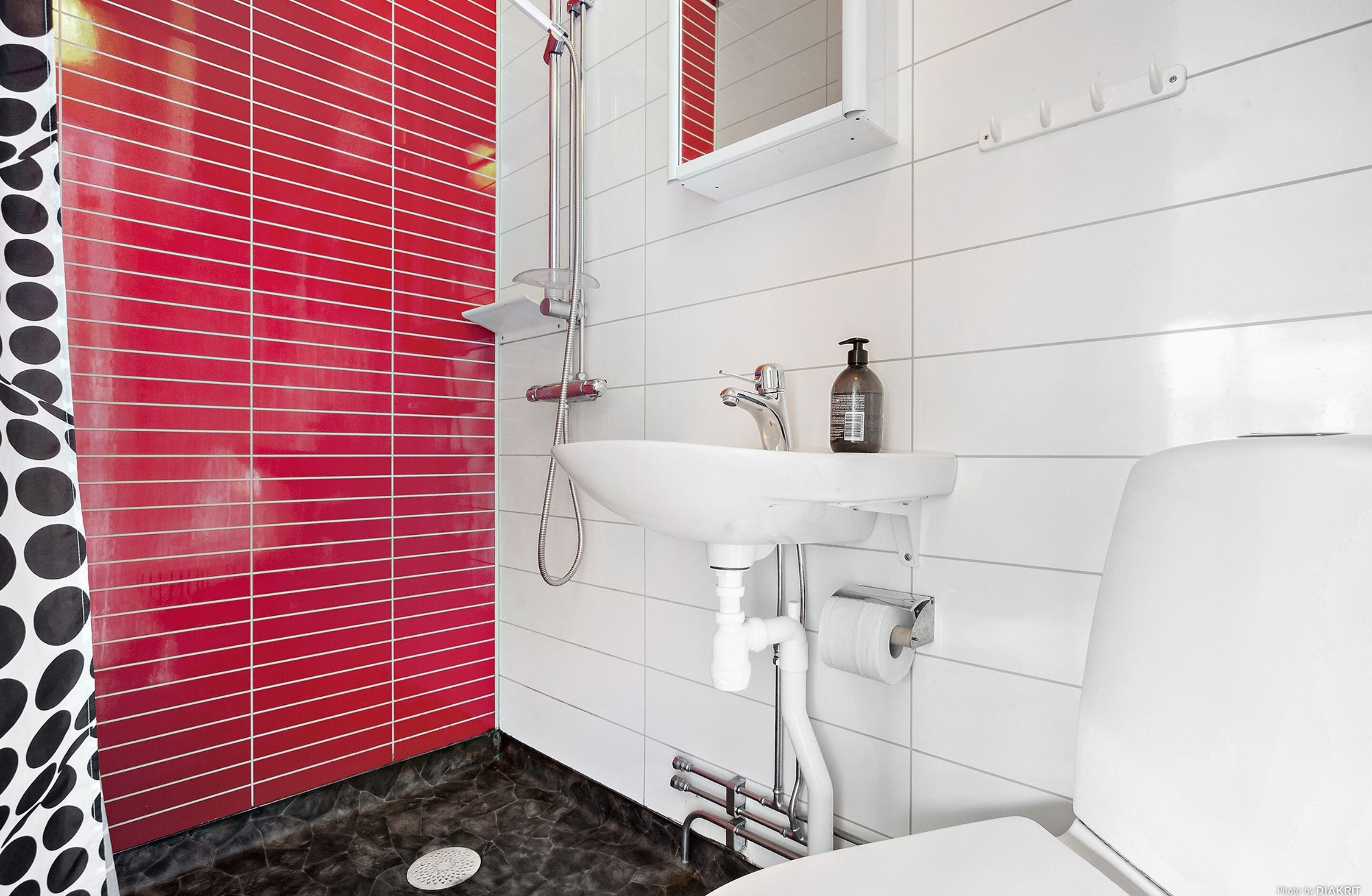 A bathroom with a white sink, red tiled walls, and a shower.