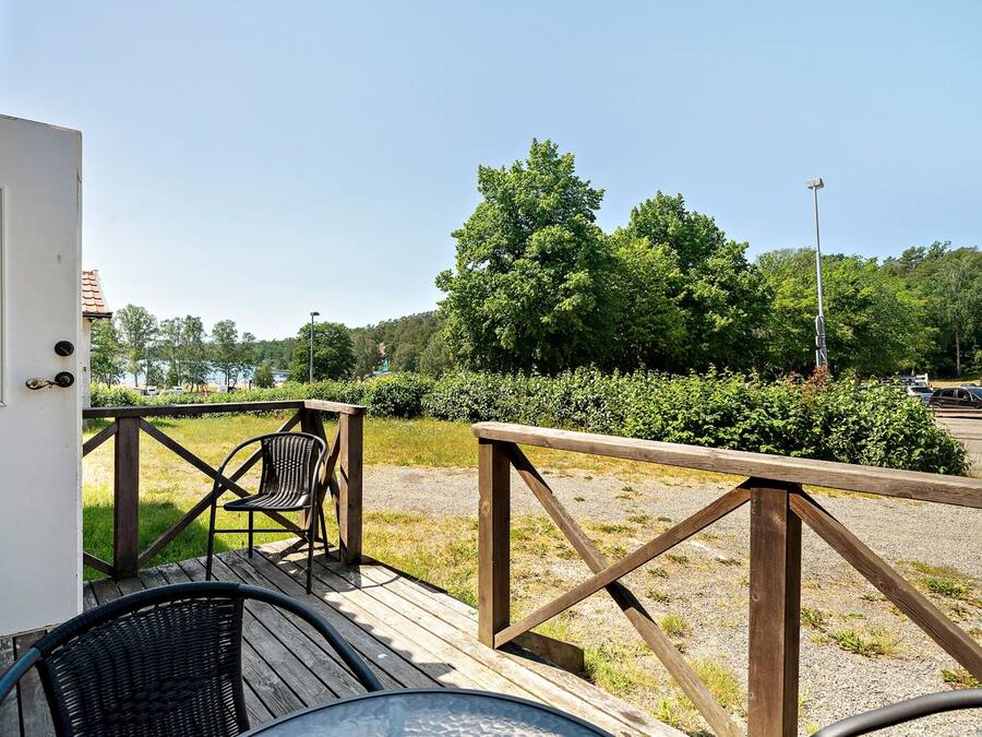 A wooden deck with outdoor seating, a view of a forested area, and a parking lot in the background.