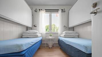 Quarto com duas camas de solteiro, uma mesinha com uma planta e uma janela com cortinas.