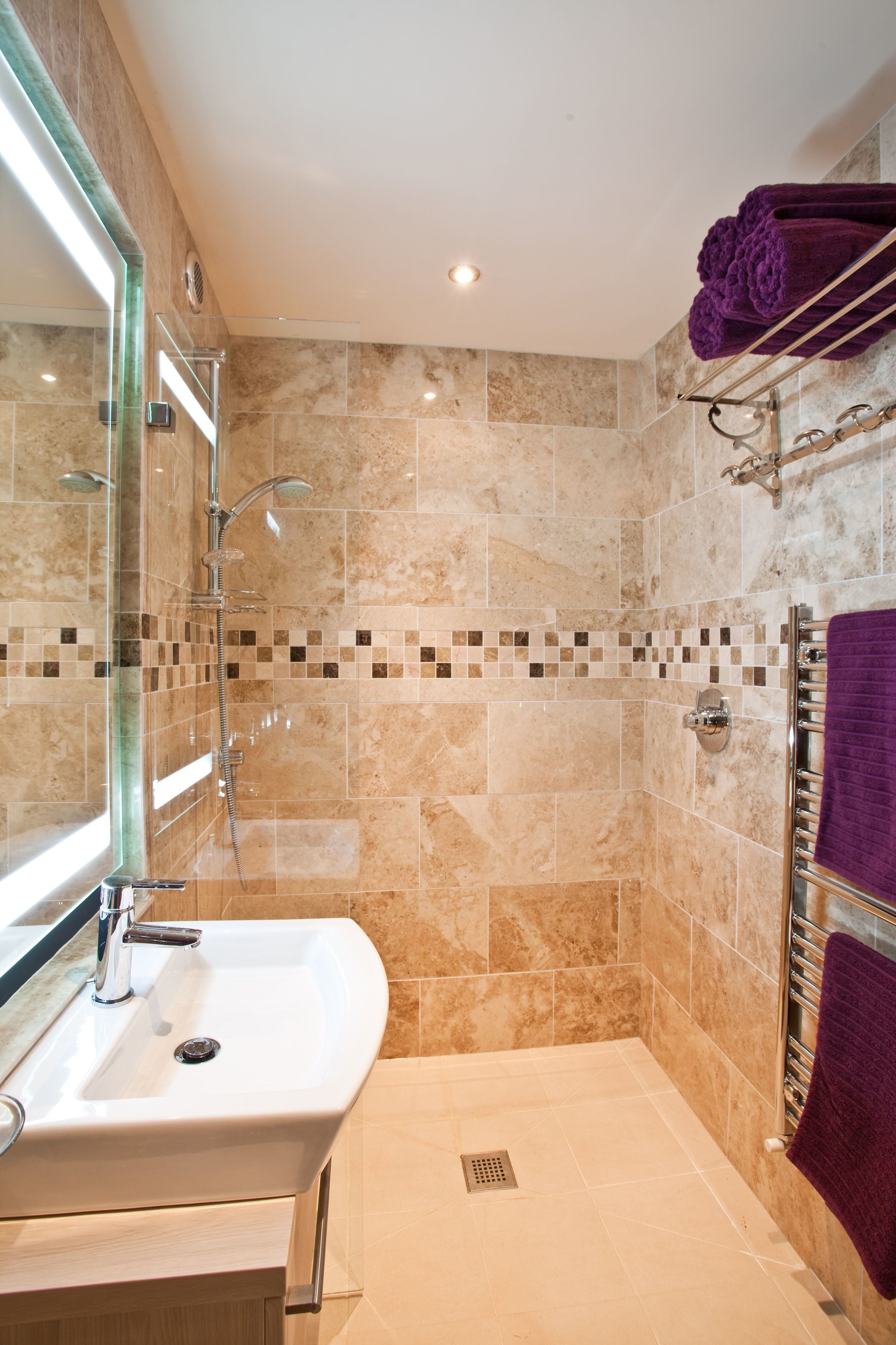 Une salle de bain moderne avec une douche à parois de verre, un lavabo avec un miroir et un porte-serviettes orné de serviettes violettes.