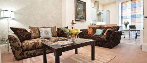 A living room with two patterned sofas, a coffee table with magazines, and a fruit bowl.