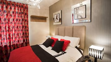 A neatly made bed with a red and black blanket, a bedside lamp, and a framed picture on the wall.
