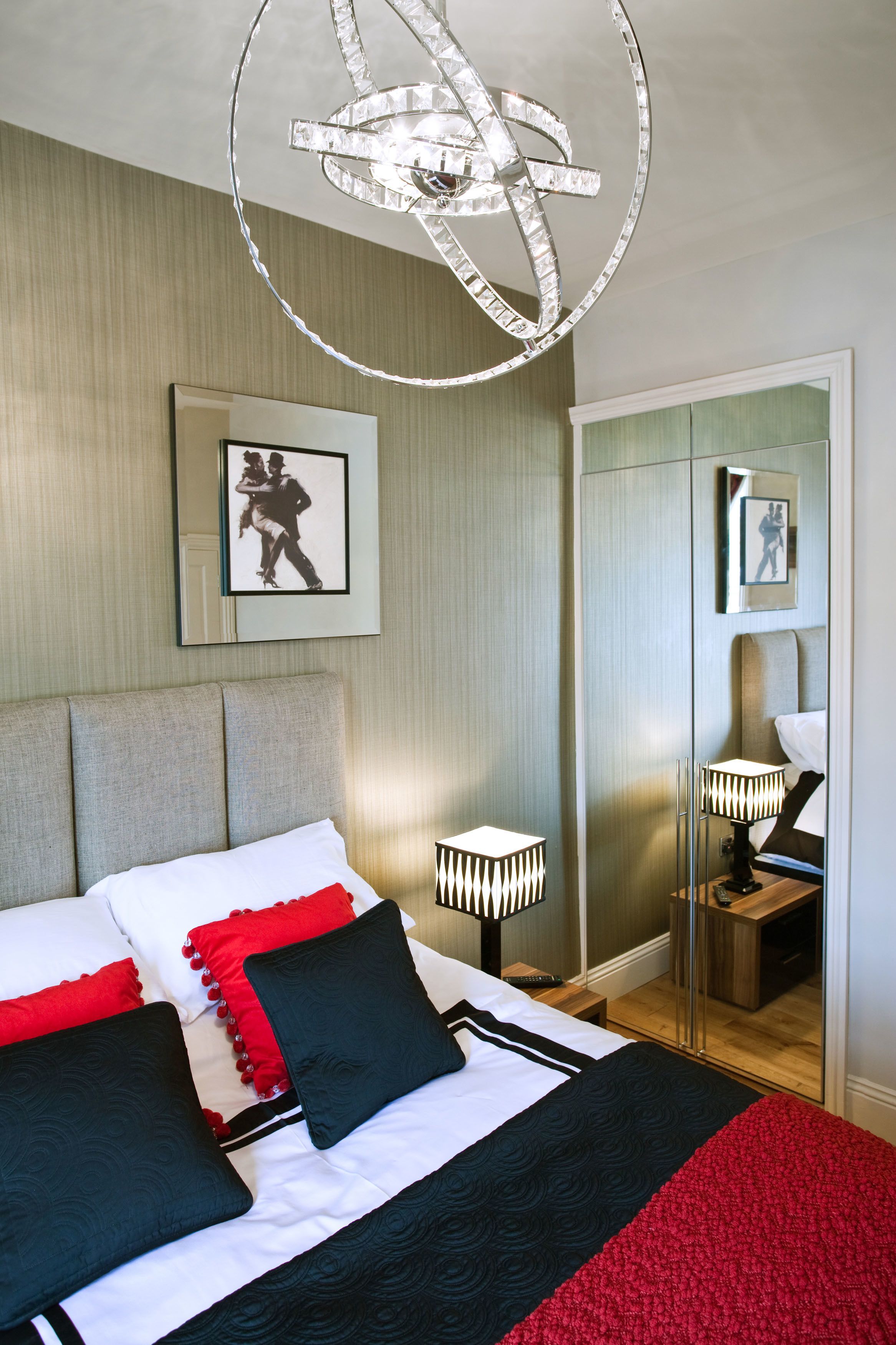Een keurig opgemaakte slaapkamer met een bed, bedlampjes, een spiegel en een ingelijst schilderij aan de muur.