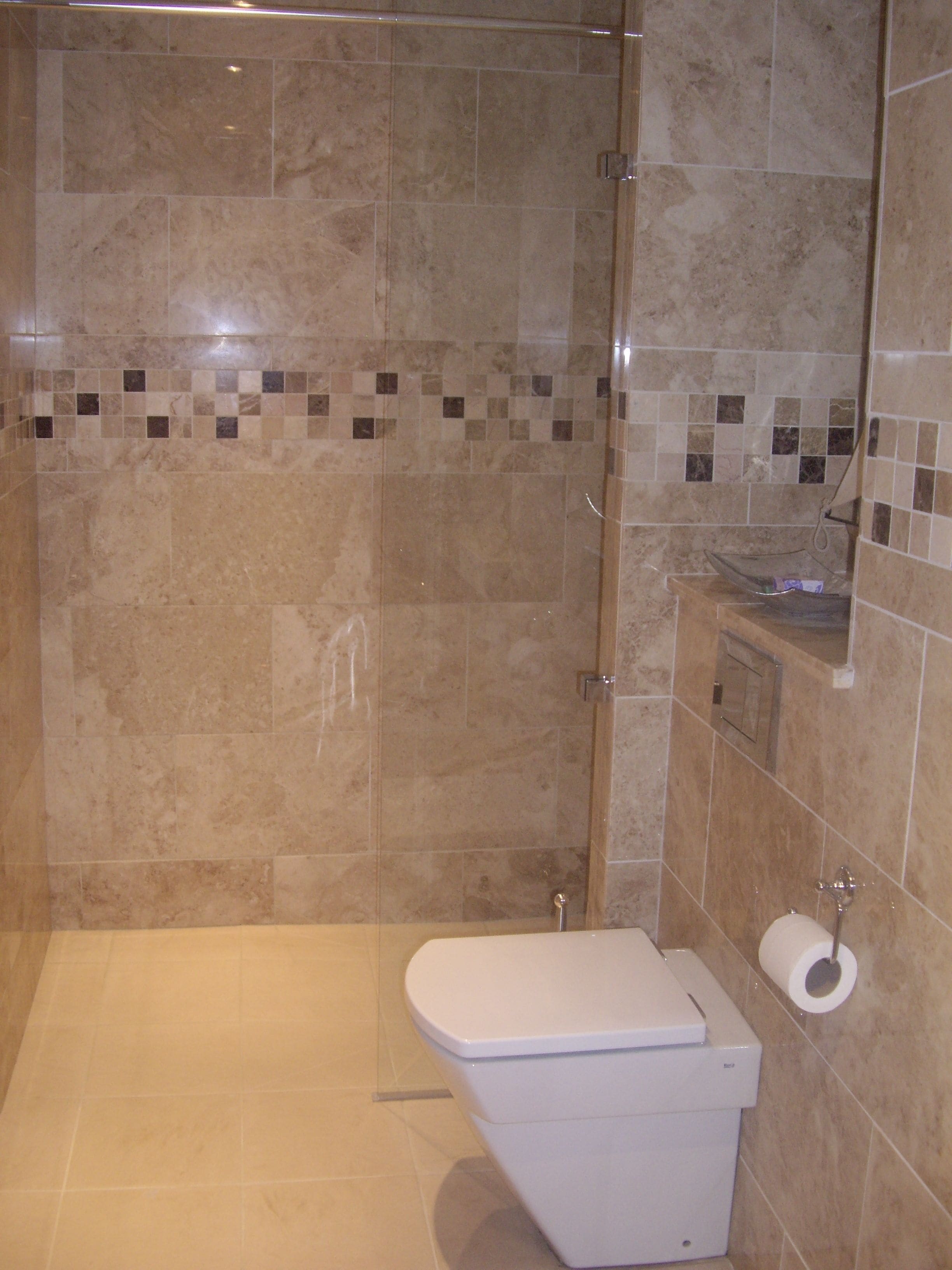 Un baño moderno con ducha envuelta en vidrio, inodoro blanco y una pequeña zona de lavamanos.