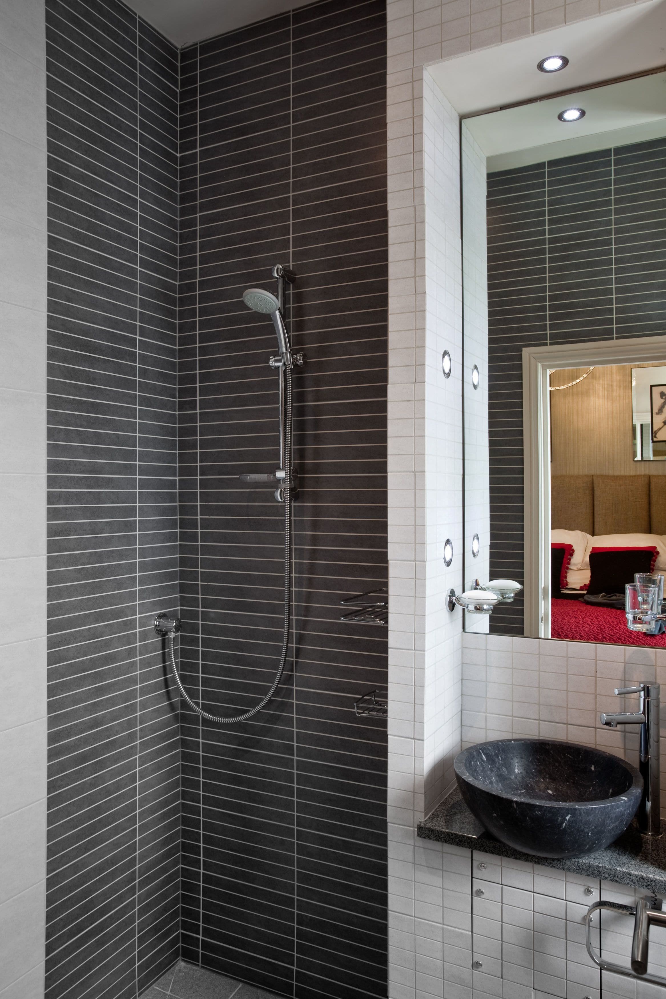 A bathroom with dark tiled walls, a black vessel sink, and a handheld showerhead.